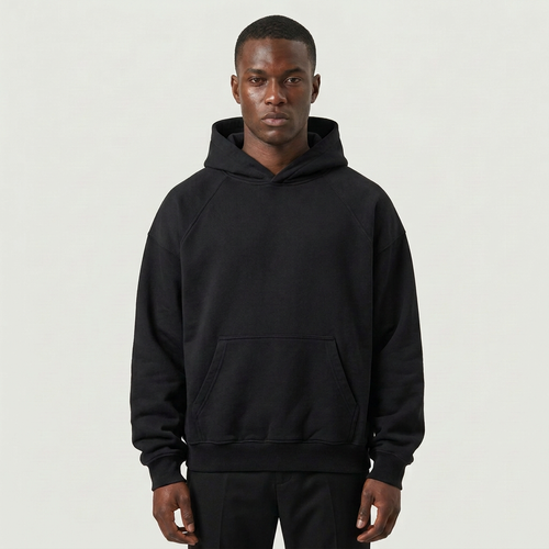 A man wearing a black pullover hoodie with a front kangaroo pocket, photographed against a plain light gray studio background.